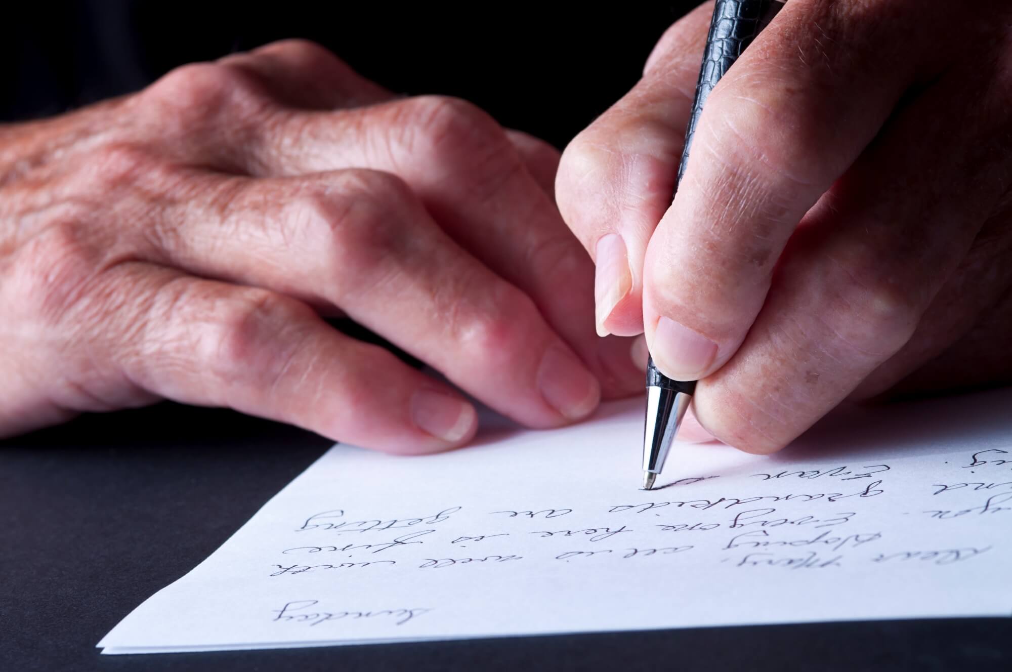 Close up photo of hands holding a pen writing a eulogy.