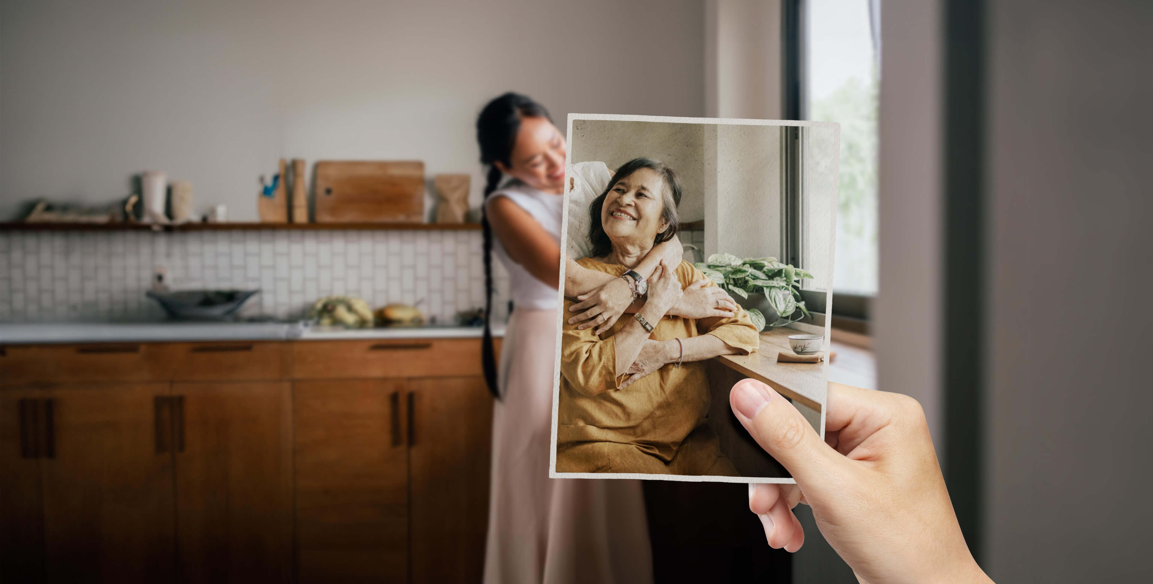 A younger woman appears to be embracing an older woman - perhaps a mother or relative. Looking more closely, we notice the older woman isn't actually in the room, but is contained within a lightly faded photograph seemingly held in position by an unseen observer..