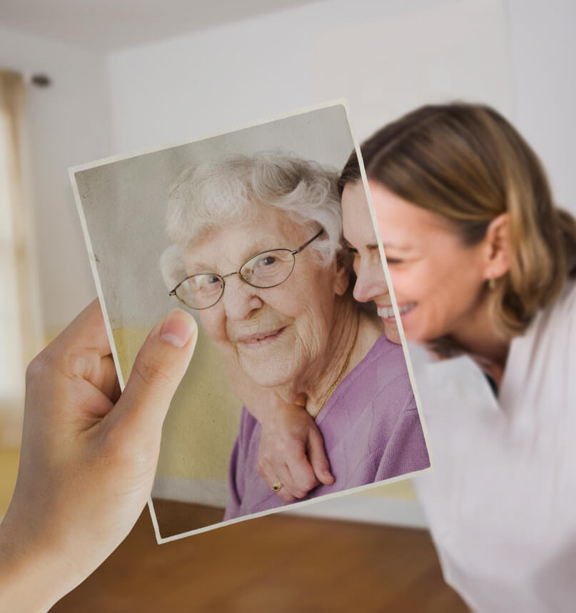 A younger woman appears to have her arm around an older woman. Looking closer, we notice the older woman is in fact in a photograph held in position by an unseen viewer.