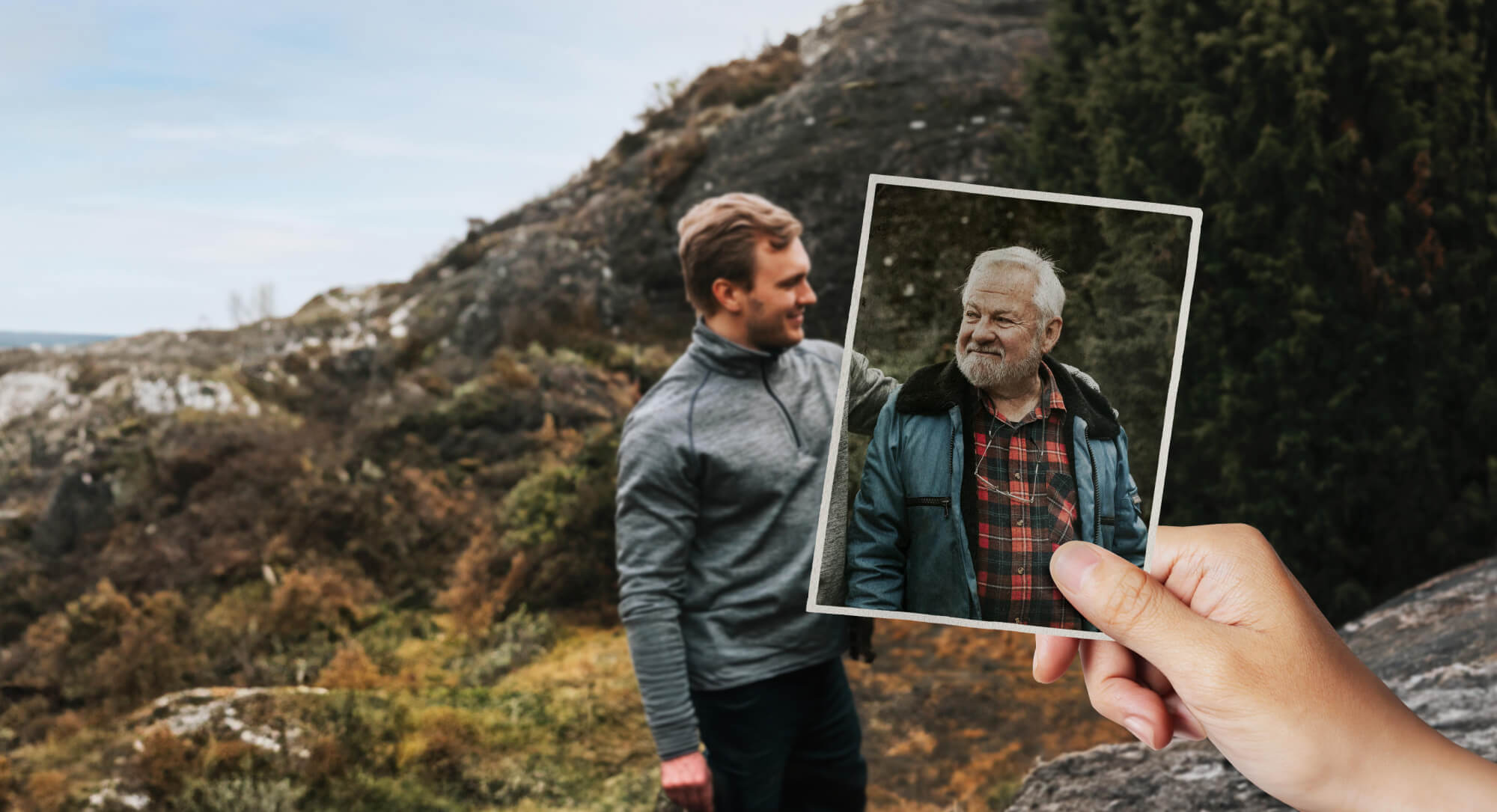 Two men appear to be hiking in rocky bushland. Looking closer, we notice the older man is actually not part of the scene, but is in fact just an aging photo held by an unseen viewer