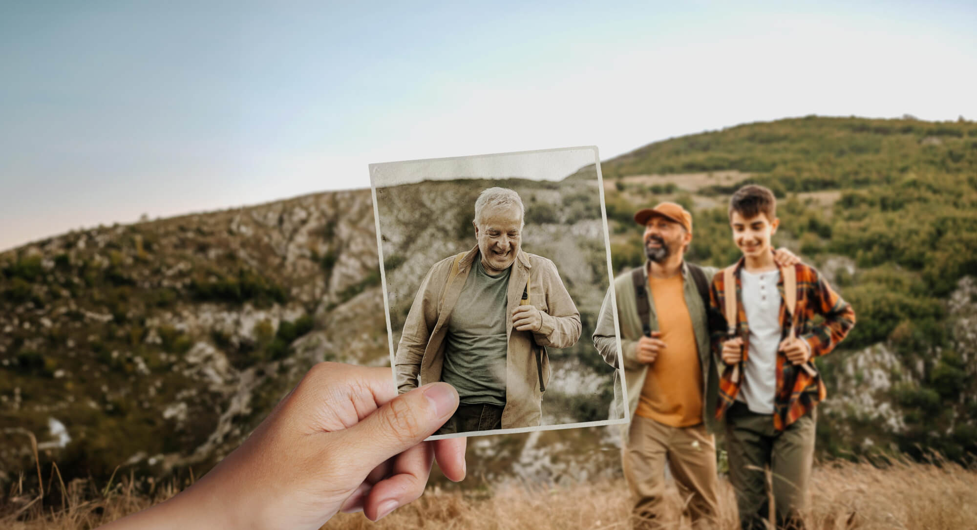 Three men from different generations appear to be hiking through rocky native bushland. Looking closer we notice that the older man isn't actually there. In fact, he is framed in an aging photograph, held in position by an unseen viewer.