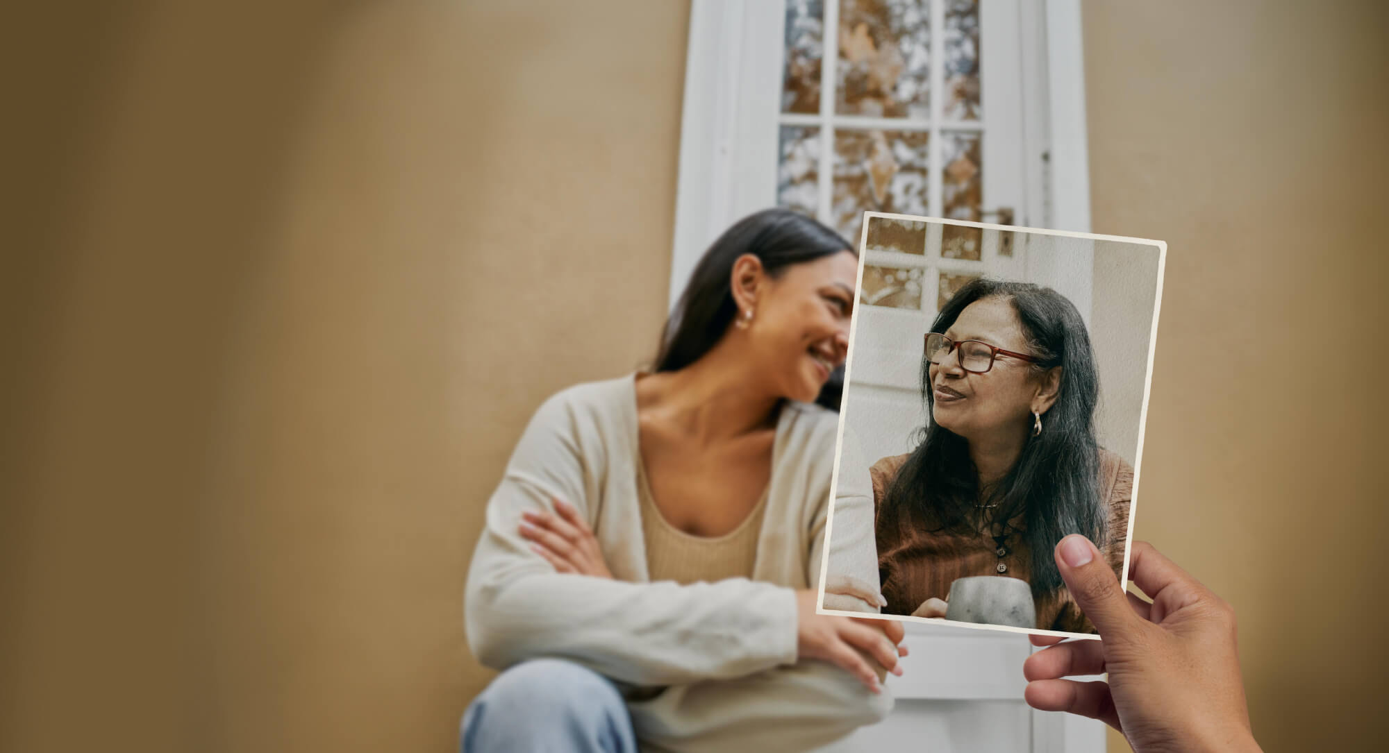 Two women share a warm moment as they sit on the front step in front of a cosy looking house. Looking more closely, we notice that the older woman is in fact only present in a photo that is held in position by an unseen observer.